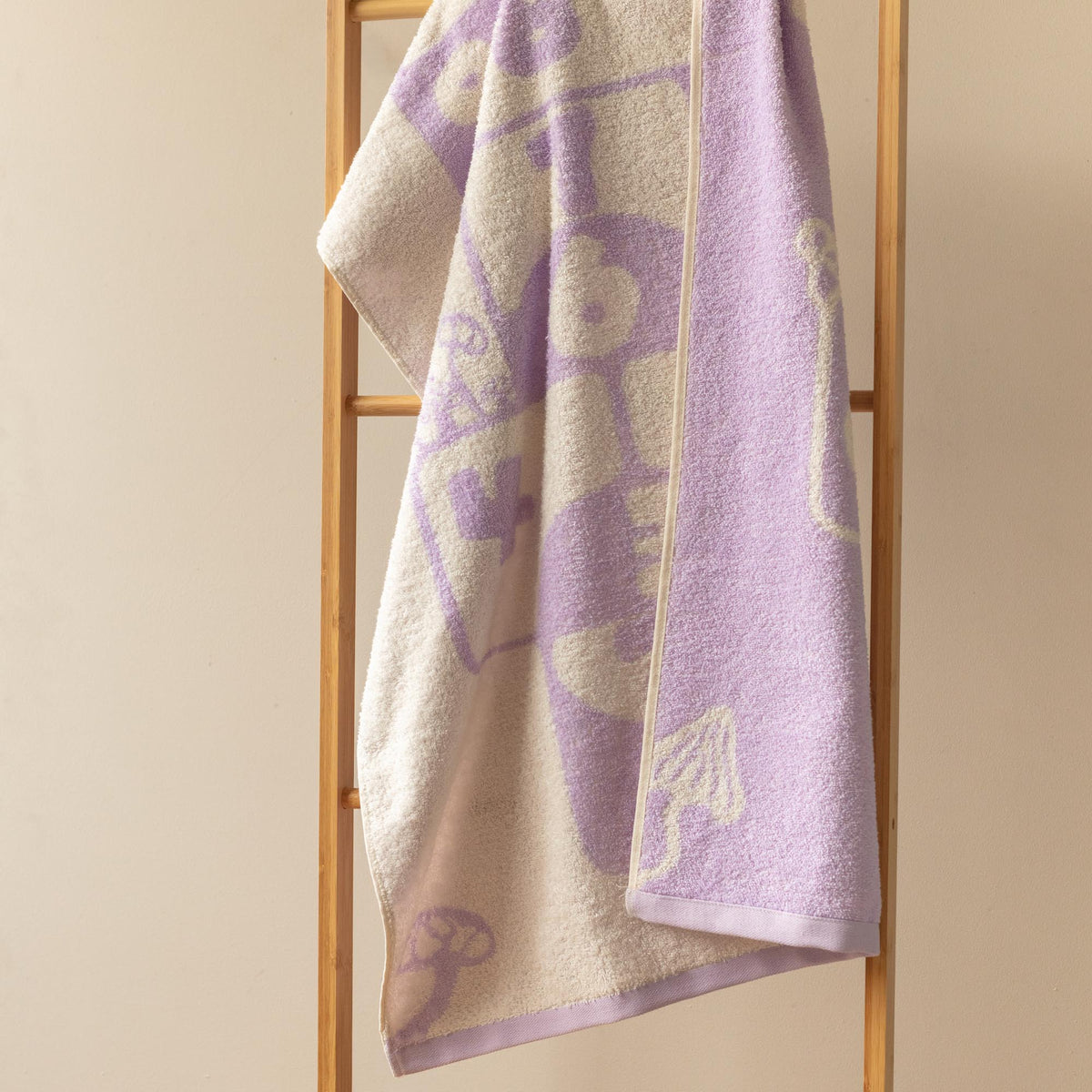 Toalla infantil Fatelares Rayuela violeta pastel y crema sobre una silla de madera